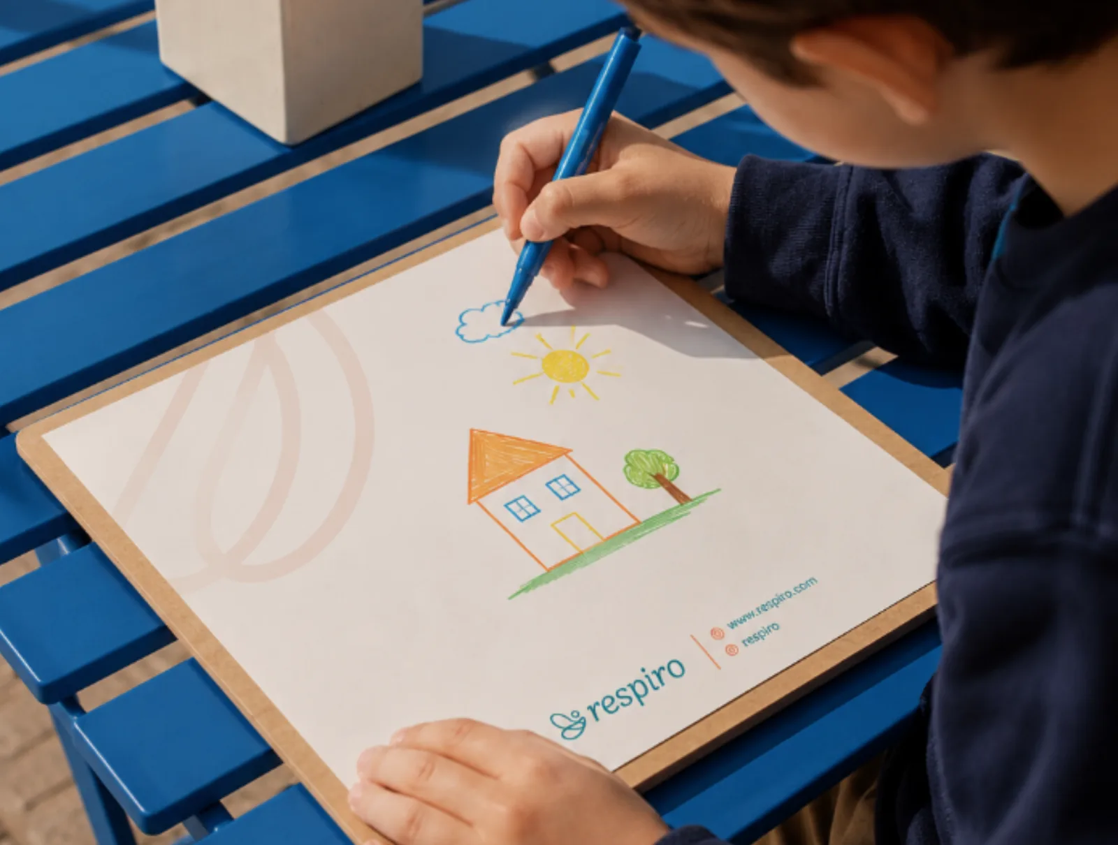 Criança desenhando uma casa em um papel com a marca Respiro.